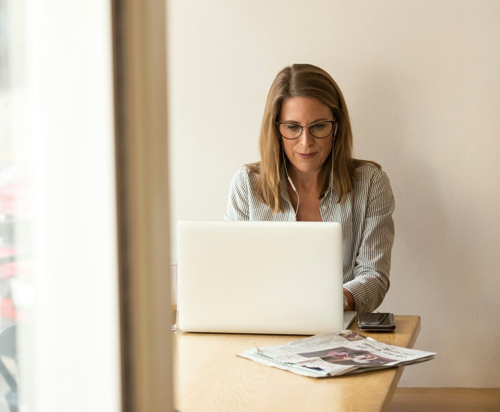 woman wearing grey striped dress shirt sitting down near brown wooden table in front of white laptop computer